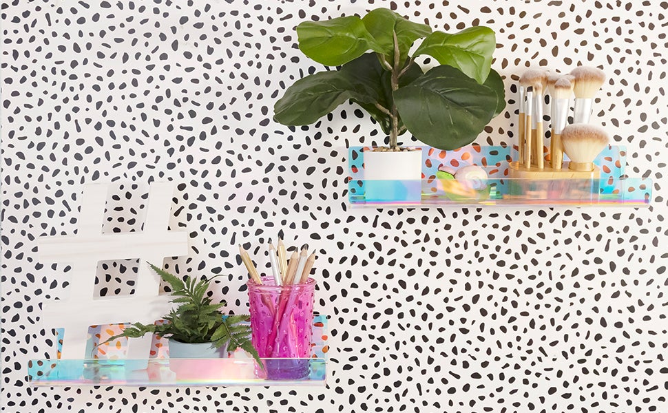 Two acrylic iridescent shelves holding random objects, on a black and white spotted wall