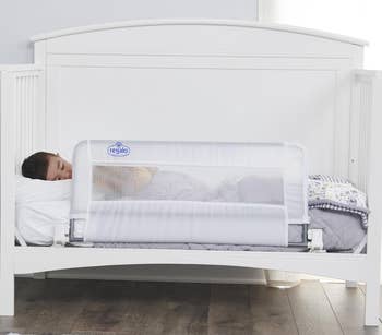 Toddler asleep in a white bed with a safety bedrail