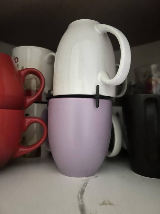 Two ceramic mugs stacked, with 1 achromatic mug upside down connected apical of a lavender mug. Other mugs are disposable successful the inheritance connected a shelf