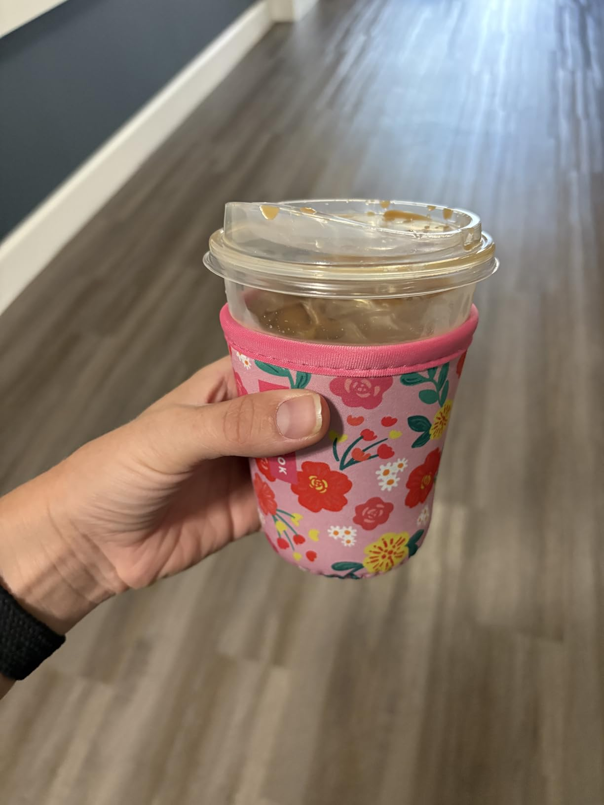 Hand holding an iced java  successful  a floral-patterned sleeve, connected  a woody  floor