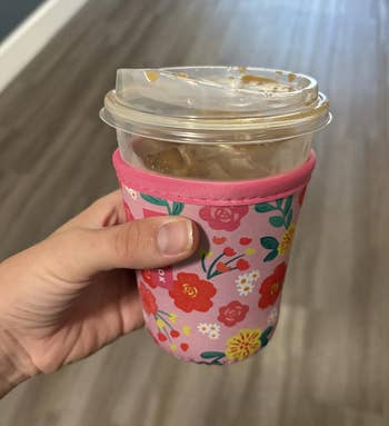 Hand holding an iced java successful a floral-patterned sleeve, connected a woody floor