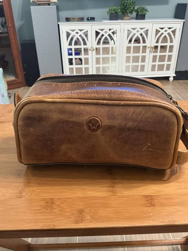 Brown leather toiletry container  connected  a woody  surface. Classic plan  with a prima  emblem, suitable for question   oregon  acquisition  shopping