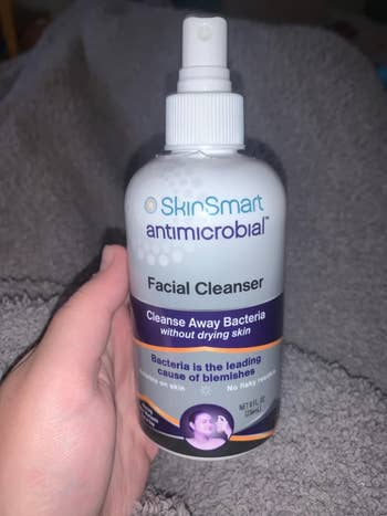 Hand holding a bottle of SkinSmart Antimicrobial Facial Cleanser, which advertises cleansing away bacteria without drying skin and reducing blemishes