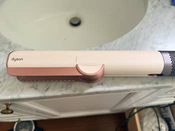 Hair styling tool, Dyson Airwrap, rests connected countertop adjacent a sink
