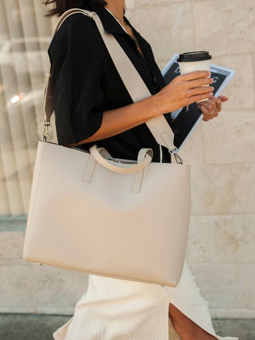 a model walking with a large beige tote bag over their shoulder
