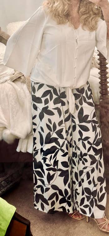 Person wearing a flowy white blouse and wide-leg pants with a bold leaf pattern standing indoors