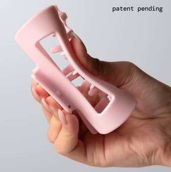 Hand holding a hairsbreadth  claw clip with a unsocial   design, labeled 