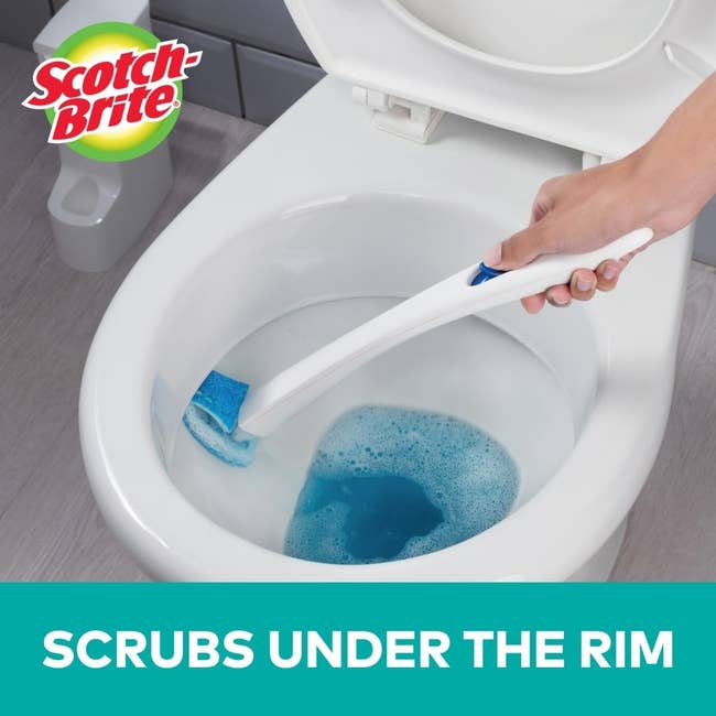 Person utilizing a Scotch-Brite toilet scrubber to cleanable  nether  the toilet rim