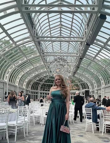 reviewer in elegant green dress standing in venue with arched glass ceiling and white chairs
