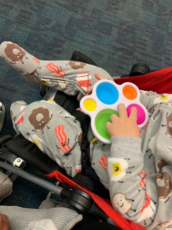reviewer's photo of their child holding the fidget toy in a stroller