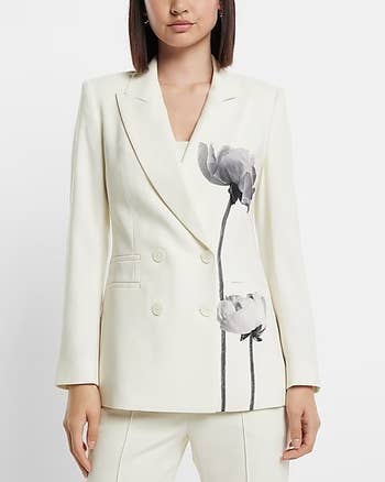 model in off white blazer with two black and gray flowers painted up one side styled with matching pants