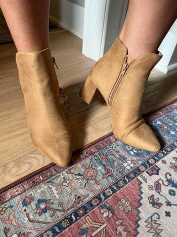 Tan suede ankle boots with artifact heels connected a patterned rug, showcasing their stylish plan suitable for buying occasions