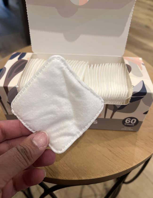 Hand holding a reusable fabric  facial pad successful  beforehand   of an unfastened  container  of akin  pads, highlighting sustainable skincare options
