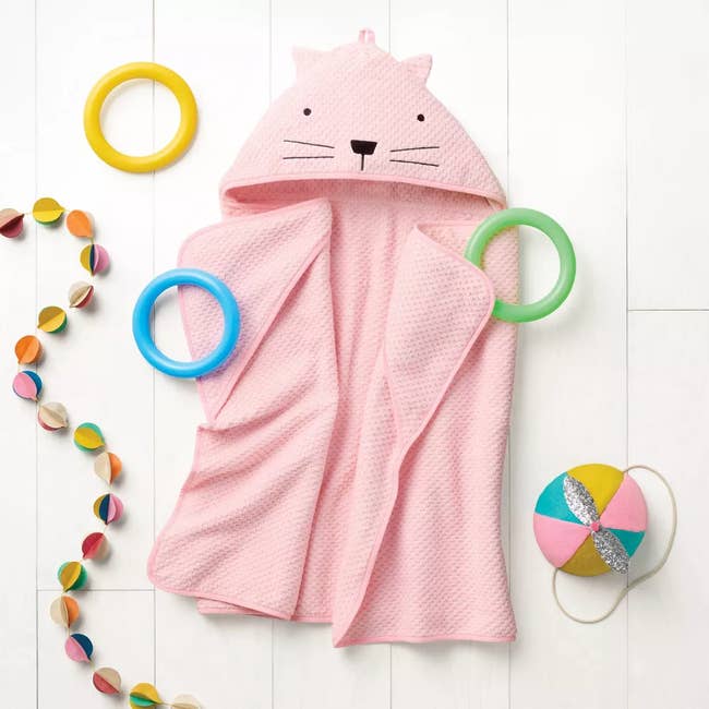 Cute pinkish  cat-themed babe  towel with hood, surrounded by colorful toys and a garland, perfect  for playful bath time