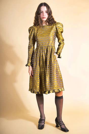 model wearing the gold dress with knee-length tights and heels