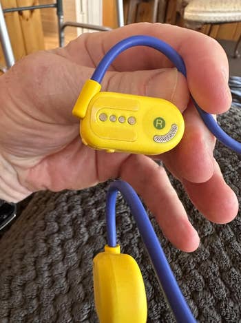 A hand holding a pair of yellow and blue wireless earbuds with a flexible neckband