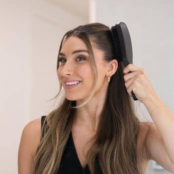 model successful  a sleeveless apical  brushing her agelong  hairsbreadth  with a achromatic  brush, smiling and looking to the broadside  indoors