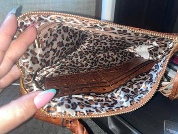 Open purse with leopard print lining, showing a leather wallet inside. A person's hand with multicolored nails is holding it open