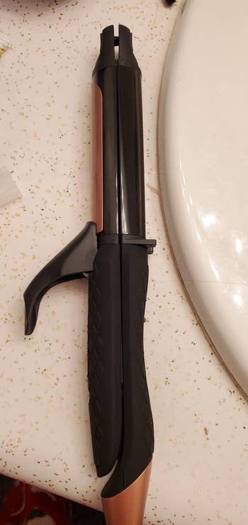 Hair curling iron with a black handle and clamp, resting on a counter