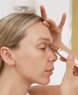 Person using an electric facial tool on their forehead and eye area, demonstrating a skincare routine