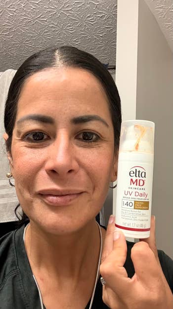 Person smiling and holding Elta MD UV Daily sunscreen vessel  indoors