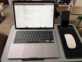 reviewer photo showing the lap desk setup with a macbook air, mouse, and phone in the phone holder