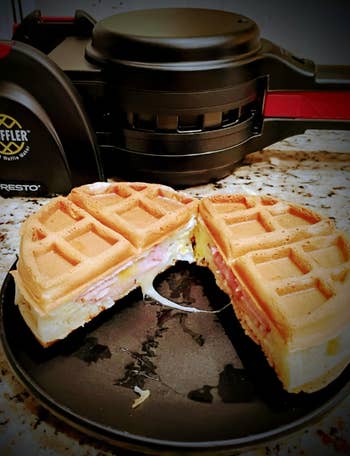 Waffle sandwich with ham and cheese on a plate next to a waffle maker