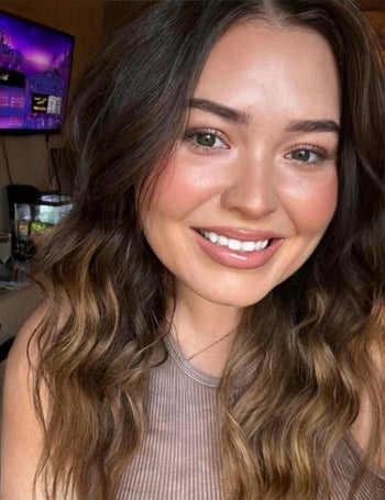 a reviewer with wavy hair smiling for a selfie, wearing a casual sleeveless top