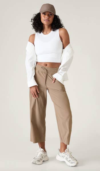 Woman in a white crop top with cold-shoulder sleeves, tan trousers, and sneakers, posing for a fashion look