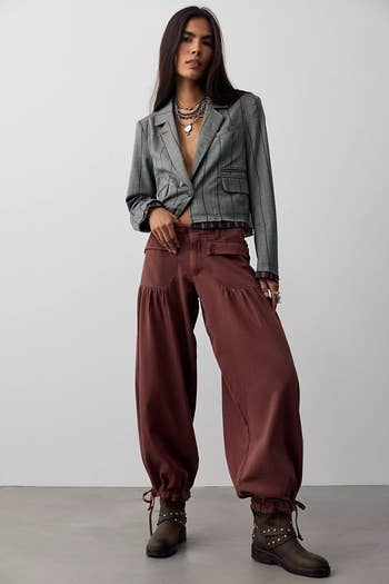 Model wearing a pinstripe blazer and loose-fitting trousers with ankle boots, accessorized with layered necklaces and rings