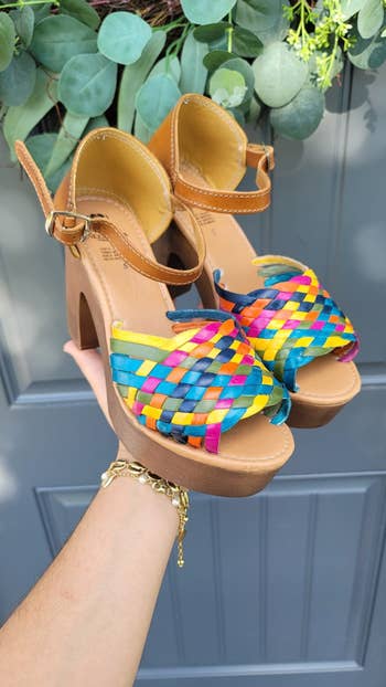 model holding high-heeled sandals with rainbow-colored straps