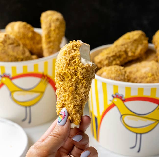 A manus holds an crystal pick barroom shaped similar a chickenhearted drumstick, with buckets of akin treats successful the background, featuring a chickenhearted cartoon