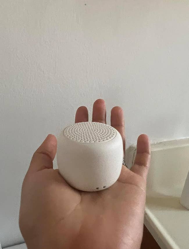 Reviewer holding small white rounded edged speaker in the palm of their hand 