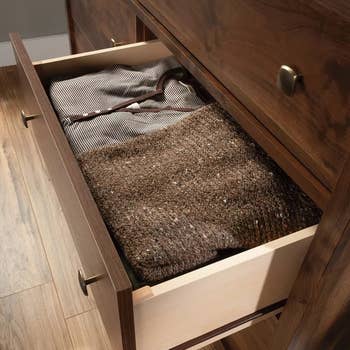 an open drawer with sweaters inside of it