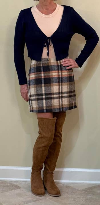 Person wearing a beige top, blue cardigan, plaid skirt, and brown knee-high boots, showcasing a casual fall outfit suitable for shopping