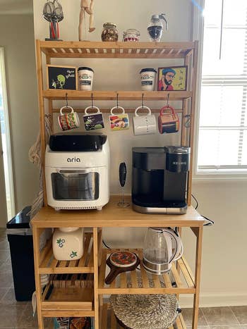A woody  room  support  holding an aerial  fryer, a Keurig java  maker, a kettle, mugs, spices, and decorative items