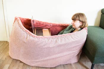 Model using a laptop while inside a pink floof that swallows their entire body as if inside a cozy pocket