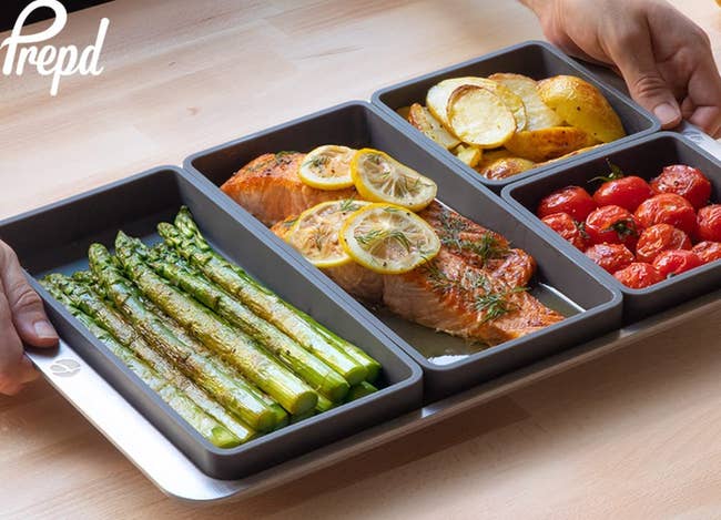 person cooking asparagus, salmon, potatoes, and tomatoes in prep'd trays