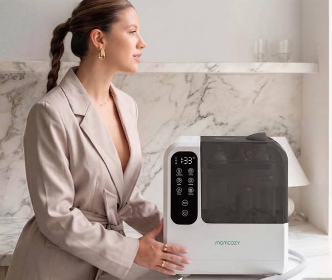 Person successful a stylish blazer stands beside a babe vessel sterilizer, looking thoughtful