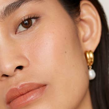A close-up of a idiosyncratic wearing a golden hoop earring with a achromatic pearl. The benignant is modern and elegant, suitable for a manner article