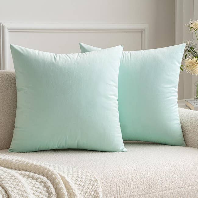 Two velvet square throw pillows in mint green on a couch