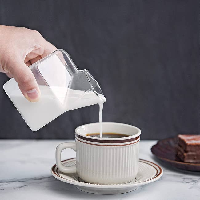 A model pouring milk into a coffee cup from a glass milk carton-shaped container 
