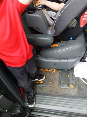 Child lasting successful car adjacent to spot covered with cracker crumbs; suggests messy car concern often associated with young children