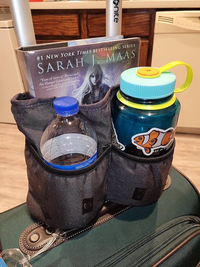 Two water bottles and a book in a holder attached to a suitcase