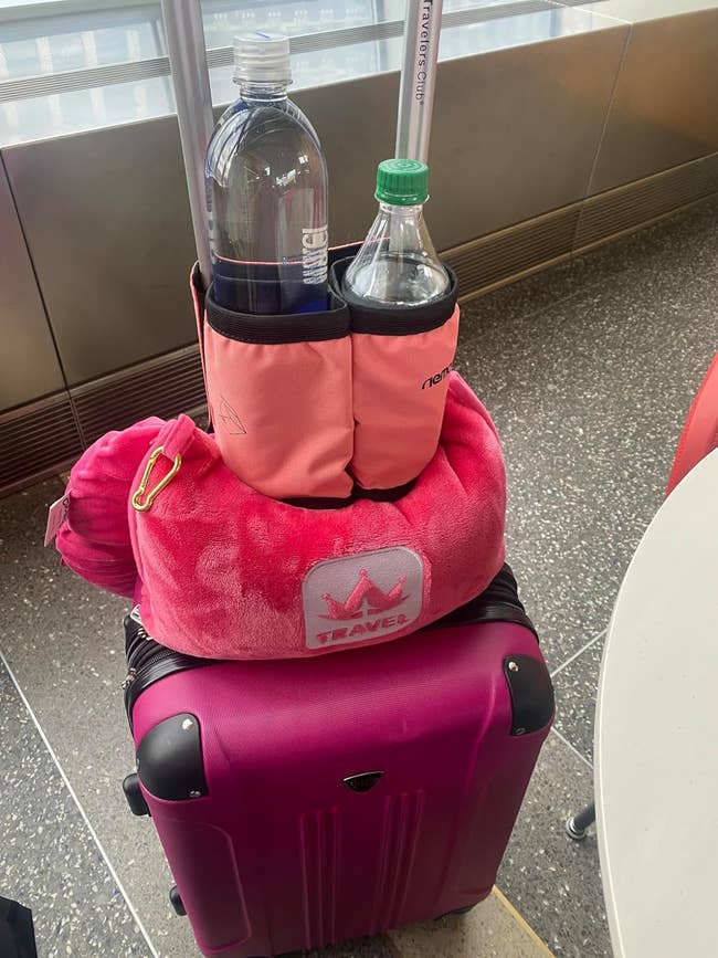 Suitcase with pink cup holder attachment containing a large water bottle and a smaller water bottle on top