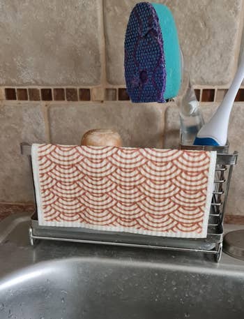 a wet Swedish dishcloth draped over the side of a sponge caddy by a sink 