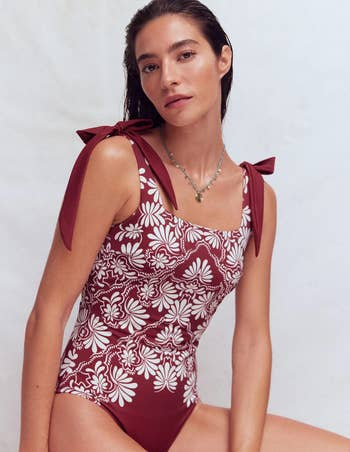 Model wearing a floral-patterned swimsuit with bow straps, sitting gracefully. Minimal constitution enhances the classy, refined style