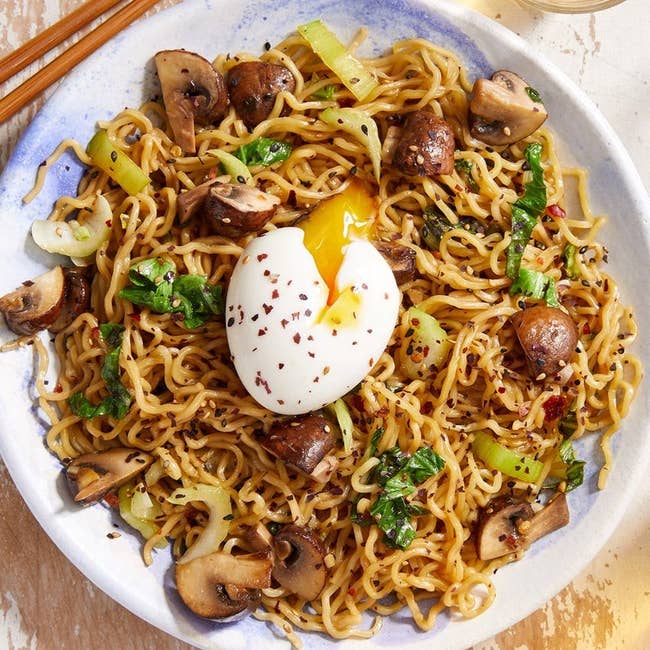 a stir fry meal with noodles, a soft boiled egg, and mushrooms