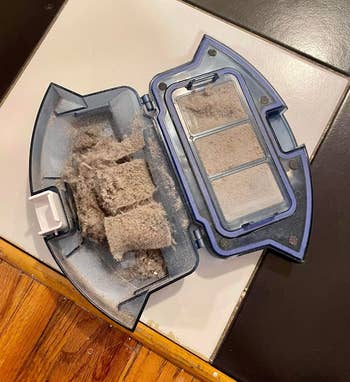 Reviewer's photo of the robot vacuum, opened and showing all the dirt it cleaned up