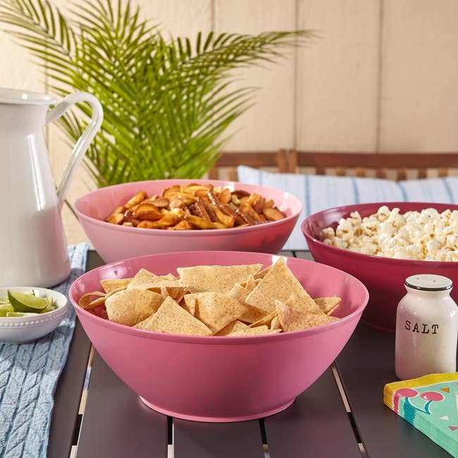 three of the pink bowls holding chips, popcorn, and a snack mix